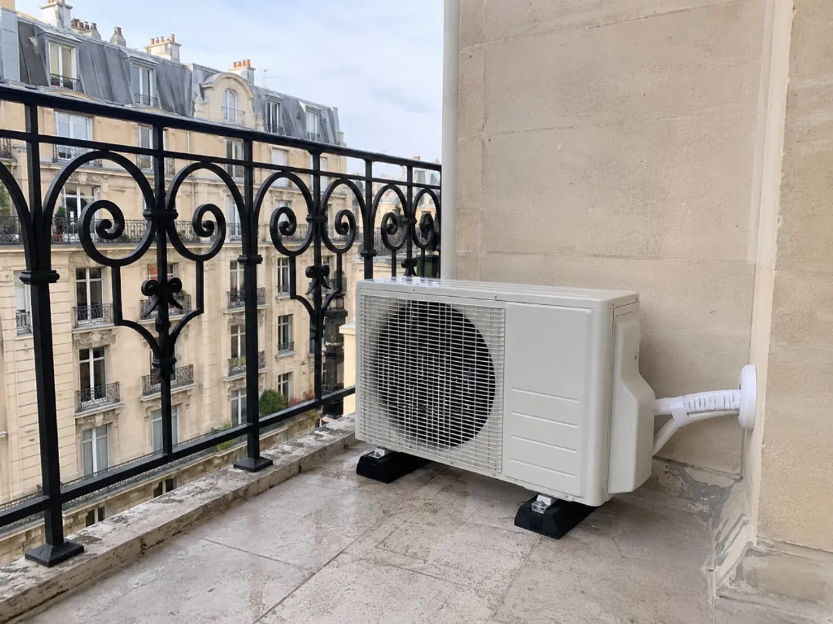 Unité extérieure de climatisation discrètement posée sur des plots anti-bruit sur un balcon à Paris